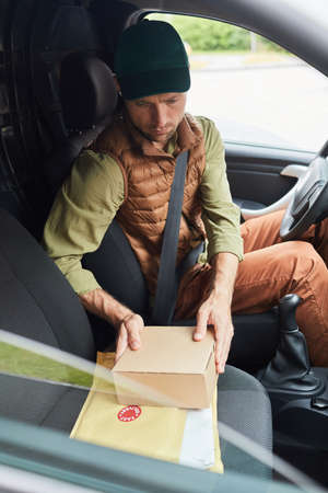 Vertical portrait of male delivery worker holding parcels while sitting in van at shipping serviceの写真素材