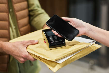 Close up of client paying for delivery service via smartphone NFC, copy space