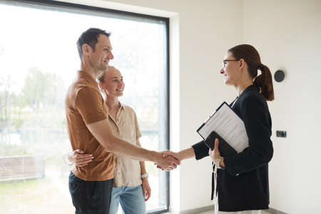 Side view portrait of young couple shaking hands with real estate agent during apartment tour, copy spaceの写真素材
