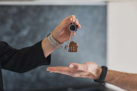 Side view close up of female real estate agent giving keys to young man buying house, copy spaceの写真素材