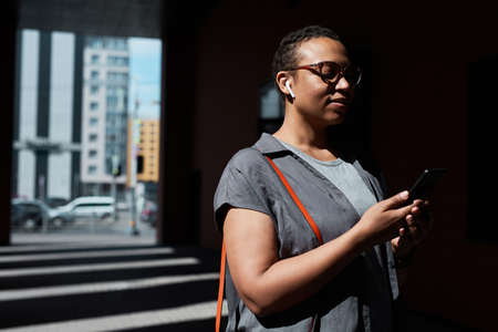 African young woman reading a message on mobile phone whie standing at office building