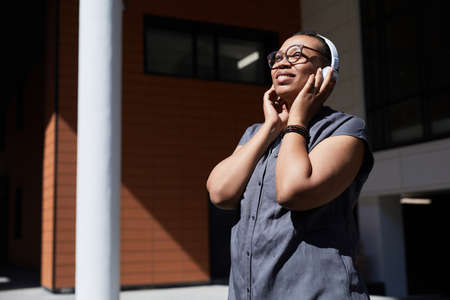 African woman in wireless headphones enjoying the music while standing outdoors