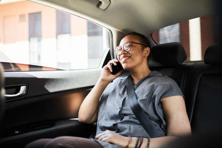 Happy African woman sitting in the car and smiling during her conversation on mobile phone