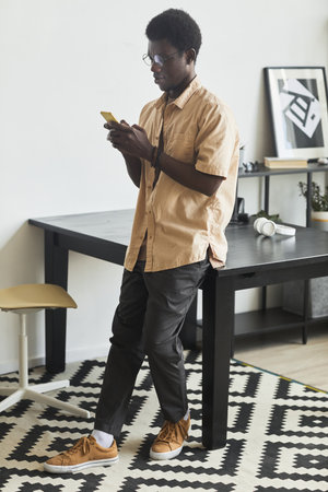 African young man leaning on the table playing online game on his mobile phone