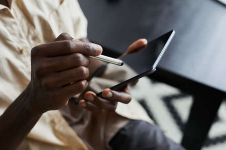 Close-up of African man holding pen and typing on touch screen of digital tablet during his online workの写真素材