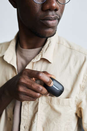 African young man in eyeglasses putting the case with wireless headphones into his pocket