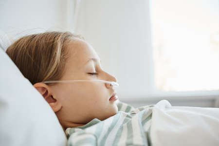 Minimal side view portrait of sleeping girl laying in hospital bed with oxygen support, copy spaceの写真素材