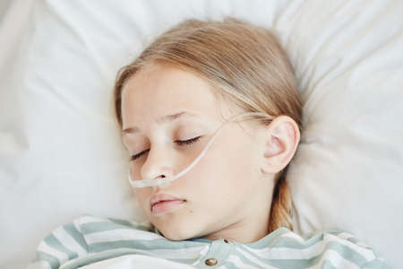 Minimal top down view at sleeping girl laying in hospital bed with oxygen support