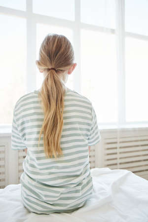 Vertical back view at lonely child sitting on bed in hospital roomの写真素材
