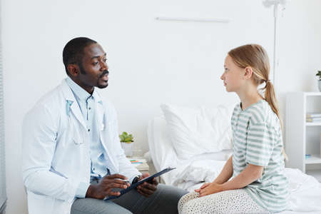 Side view portrait of African-American doctor talking to girl in hospital room, copy space