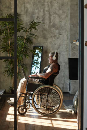 Vertical full length portrait of contemporary tattooed woman with disability listening to music while relaxing at homeの写真素材