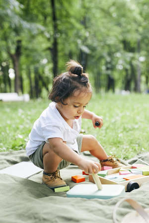 Vertical portrait of cute little boy playing with toys in park while sitting on green grass and enjoying Summer outdoorsの写真素材