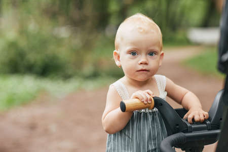 Portrait of cute baby girl looking at camera with blue eyes while enjoying walk in park, copy space