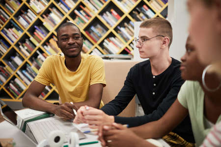 Diverse group of young people studying together at table in college library, focus on smiling African-American manの写真素材