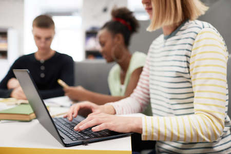 Close up of students working at table in college library focus on young woman typing in foreground, copy spaceの写真素材