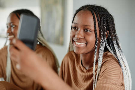 Portrait of young African-American woman video chatting with friends via smartphone and smilingの写真素材