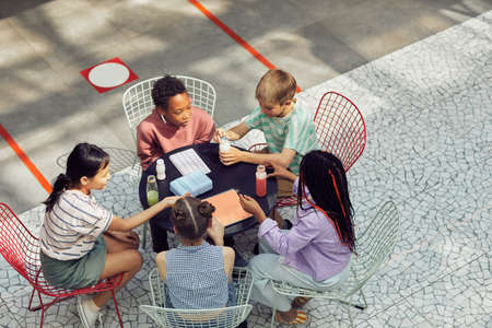 High angle view at diverse group of kids sitting at table outdoors during lunch at modern school,...
