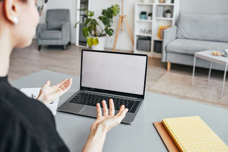 Close up of unrecognizable woman in online meeting gesturing while looking at blank laptop screen in...