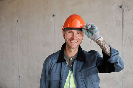 Portrait of smiling construction worker wearing hardhat while posing against concrete wall, copy...