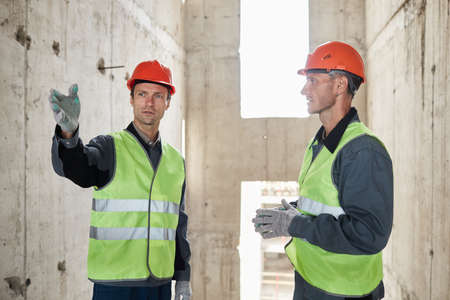 Waist up portrait of two engineers at construction site pointing away