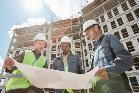Low angle view at diverse group of engineers discussing floor plans at construction site
