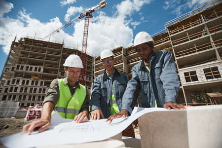 Low angle portrait of three workers discussing floor plans at construction site, copy spaceの写真素材