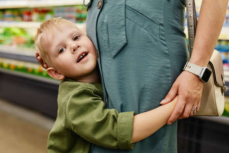 Portrait of happy loving blond-haired son embracng pregnant mother who stroking his head in shopの写真素材
