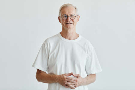 Waist up portrait of smiling senior man looking at camera while standing against white background, copy spaceの写真素材