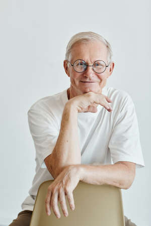 Minimal vertical portrait of smiling senior man wearing glasses and looking at camera against white backgroundの写真素材