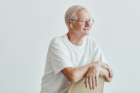 Minimal portrait of smiling senior man with wireless earphones looking away against white background, copy spaceの写真素材