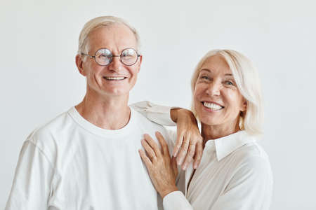 Minimal portrait of modern senior couple wearing white against white background and smiling at...