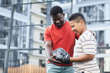 Happy middle-aged black father showing hand position while teaching son to play baseballの写真素材
