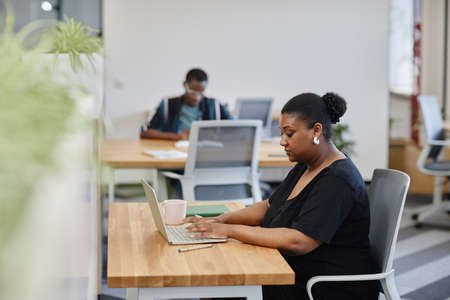 Portrait of serious businesswoman working on laptop and answering e-mails of colleagues and customersの写真素材