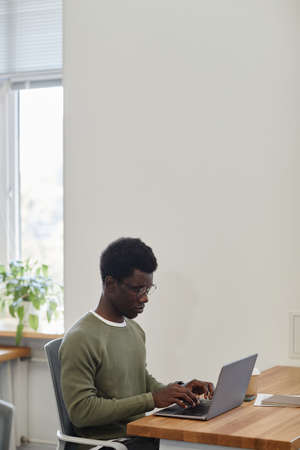 Frowning serious young businessman working on laptop at office desk and answering e-mails of...