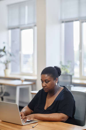 Portrait of serious female entrepreneur working on laptop at desk in modern office, filling forms onlineの写真素材