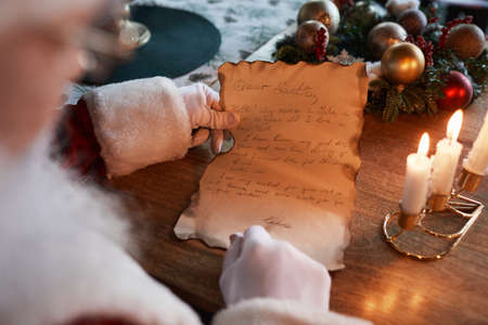 Over shoulder view of unrecognizable Santa Claus in white gloves sitting at table with burning...