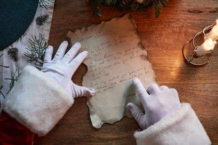 Above view of unrecognizable Santa Claus in white gloves running finger under words while reading letter at tableの写真素材