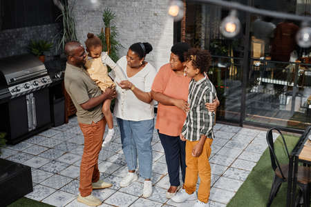 Full length portrait of modern African-American family chatting at terrace during barbeque party outdoors, copy spaceの写真素材