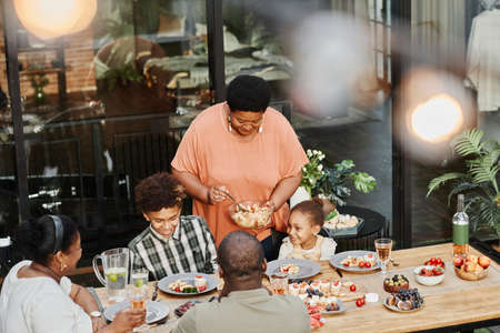 Portrait of senior African-American grandma serving food at family dinner outdoors, copy spaceの写真素材