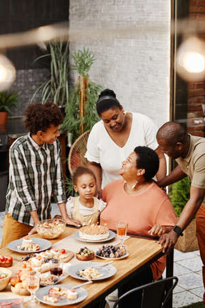 Vertical portrait of senior African-American woman celebrating birthday with family and blowing candles on Birthday cakeの写真素材