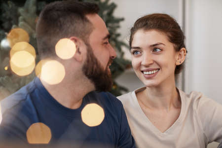 Happy young Caucasian woman looking with love at boyfriend while they celebrating Christmas together, lens flareの写真素材