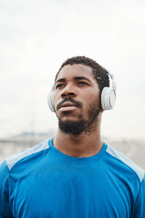 Close-up of African young man in wireless headphones looking away while training on fresh airの写真素材
