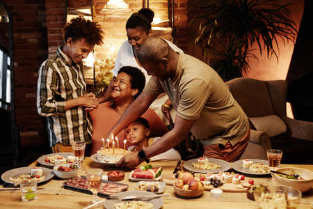 Warm toned portrait of happy African-American family celebrating Birthday together indoors at eveningの写真素材