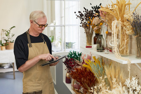 Portrait of modern senior man doing stock inventory while working in florists shop, copy spaceの写真素材