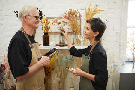 Waist up portrait of modern mature couple using tablet while working in flower shop, small business conceptの写真素材