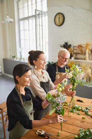 Vertical side view portrait of three florists arraigning flower compositions in cozy workshopの写真素材