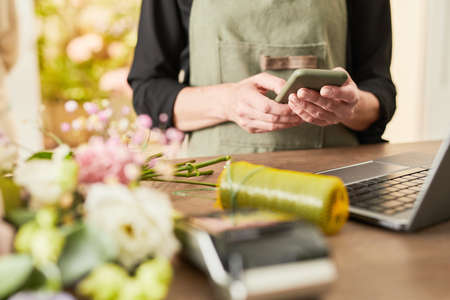 Cropped portrait of female small business owner using smartphone while managing flower shop, copy spaceの写真素材