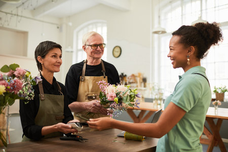 Portrait of mature couple handing bouquet to smiling female customer while working in flower shop, copy spaceの写真素材