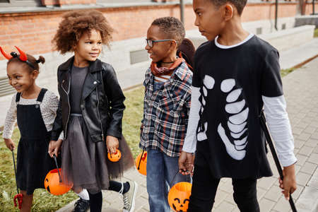 Group of excited African-American kids wearing Halloween costumes outdoors while trick or treating togetherの写真素材