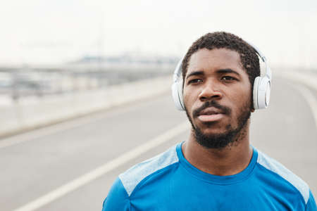 African young man putting on wireless headphones and listening to music during running outdoorsの写真素材